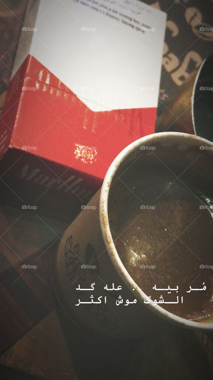A small cup of coffee with marlboro red cigarettes and an iraqi writing that means stay in touch with me as much as i miss you not more than that .