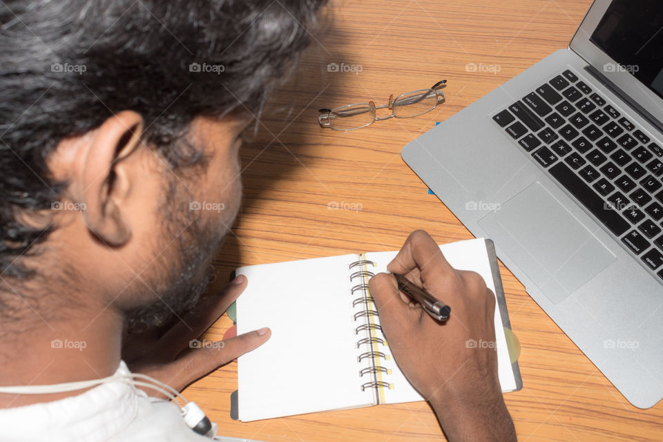 Businessman writing in his diary. Open notebook with blank pages next to cup of coffee and eyeglasses on wooden table. Business still life concept with office stuff on table. Top view with copy space.