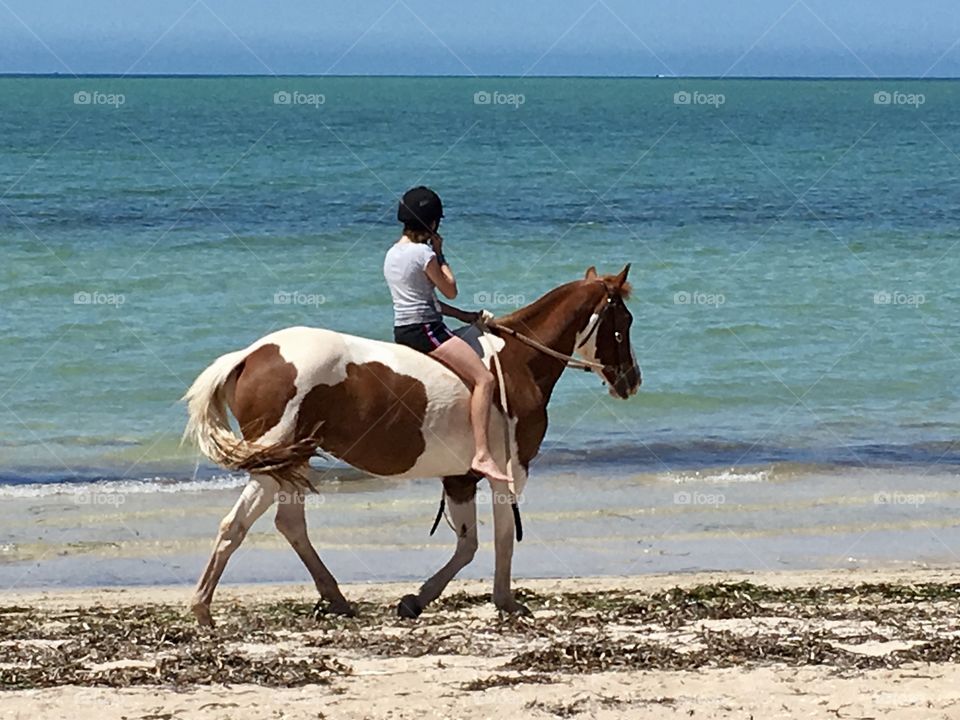 Barefoot girl riding horse along seashore 