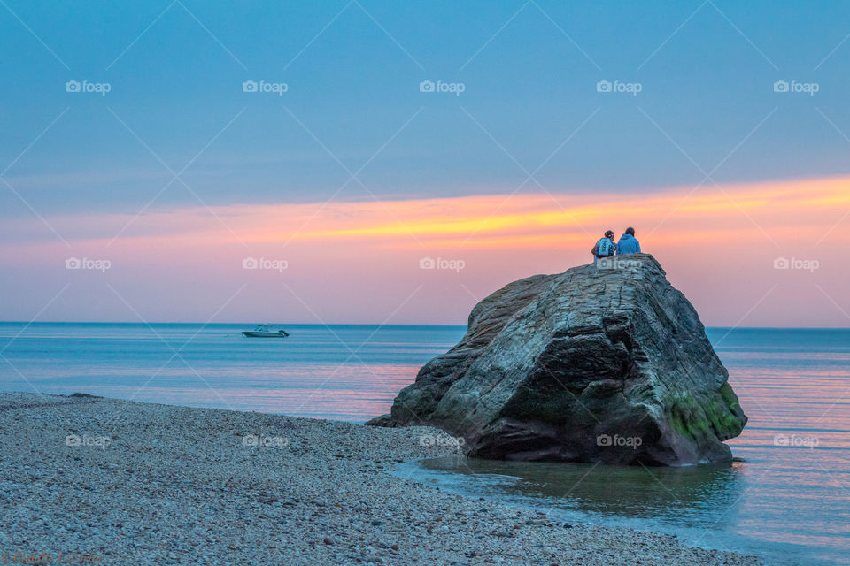A couple watches the sunset on top of a big rock on Cinco de Mayo on Long Island in New York 