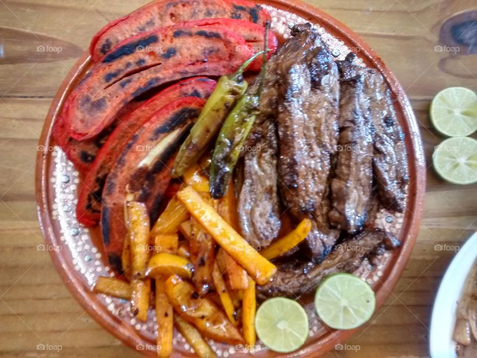 Mexican barbecue. this is a dish with a mexican barbecue, it has arrachera, bell peper, fried onion, sausages and  limes.