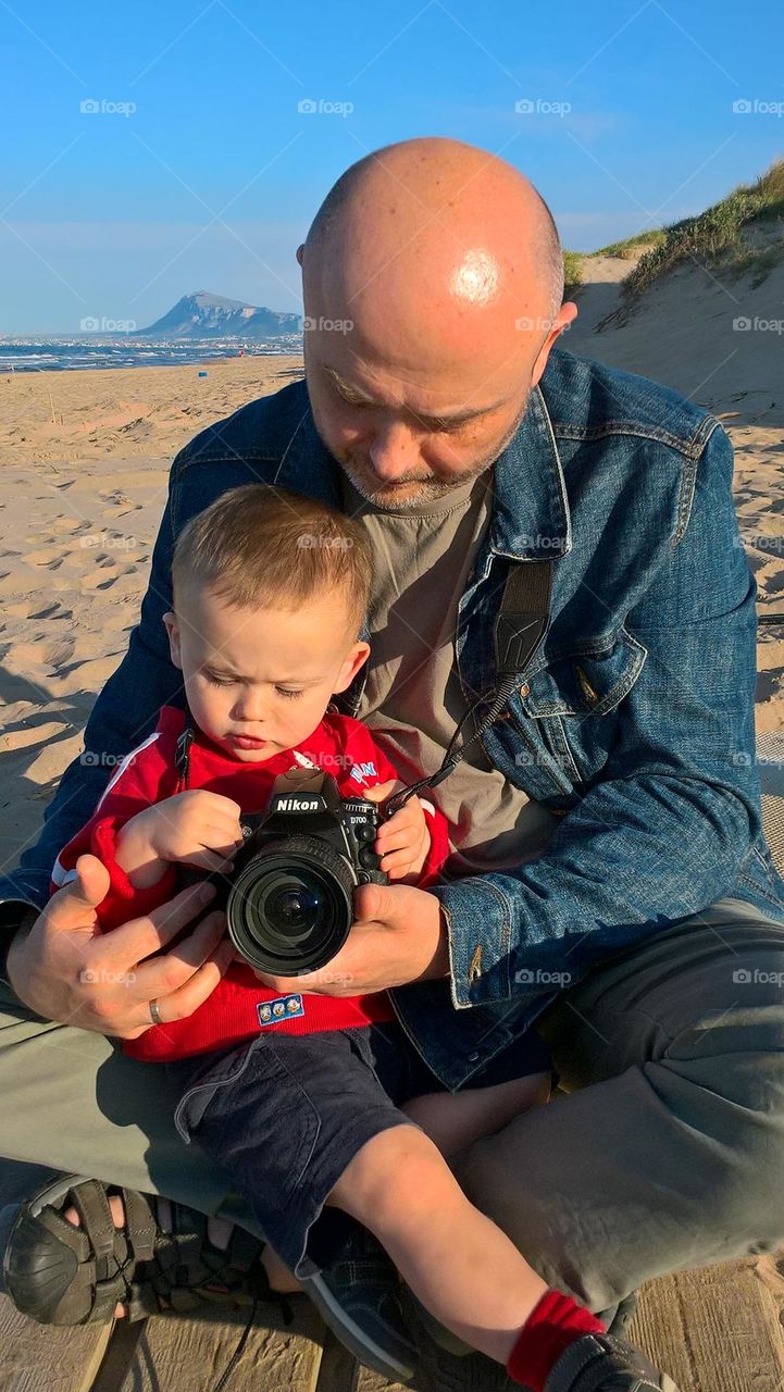 Boy learning from his parent how to use camera to take pictures.