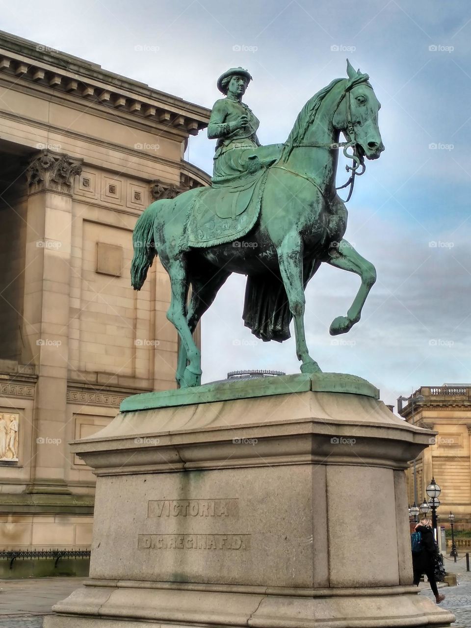 A statue of Elizabeth on a horse in Liverpool, England.  In the background city buildings and a cloudy sky.