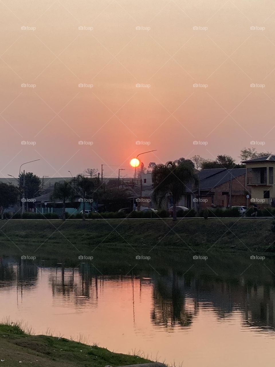 Por do sol com presença de árvores refletido num lago.