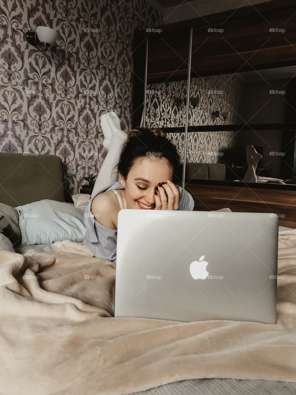 Dark hair beautiful Girl is using MacBook Air lying on a bed and smiling and laughing 