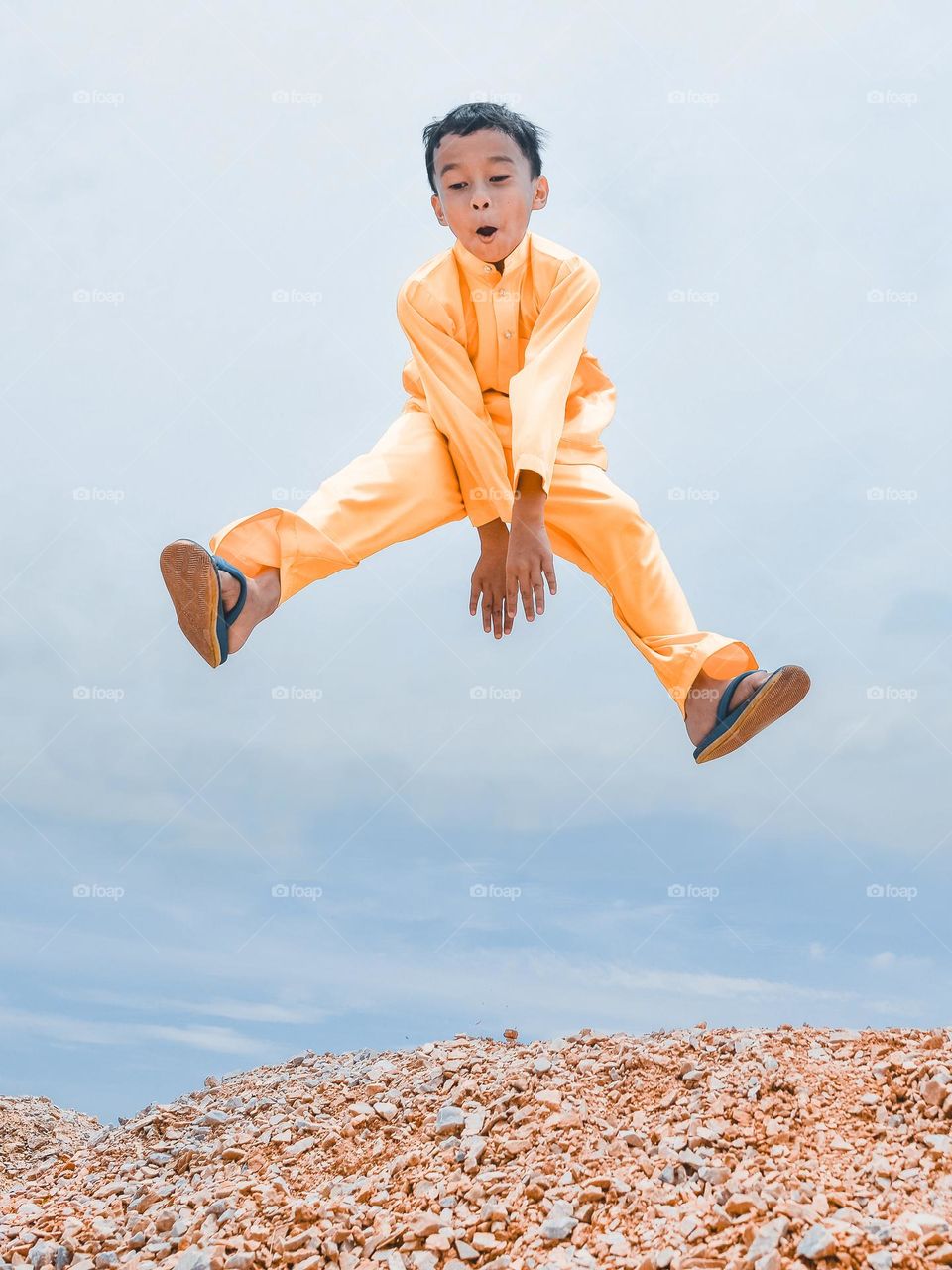 A boy in yellow happy celebrating against blue sky on a sunny day