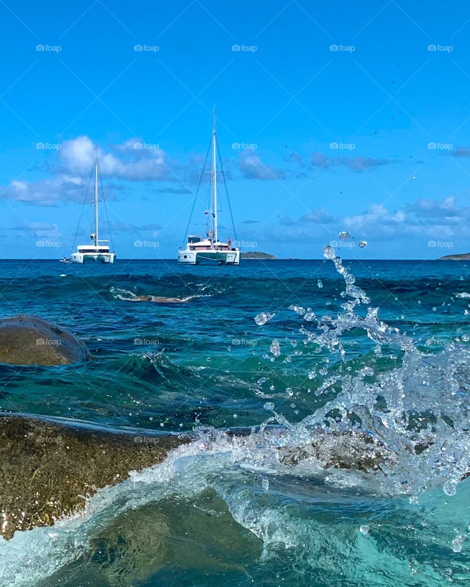 Two boats in the ocean by the beach with waves crashing