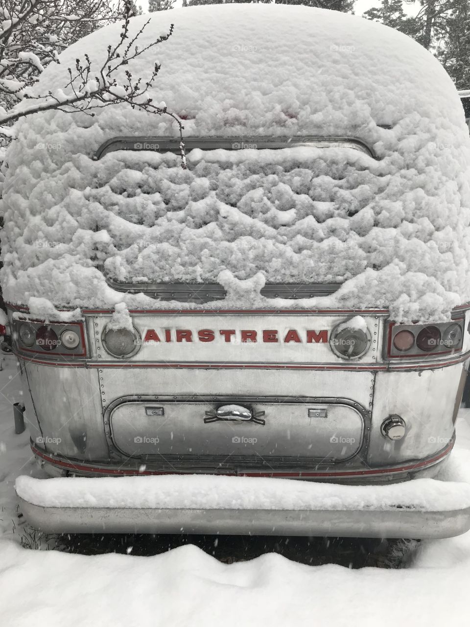 A snow covered airstream bus parked in the lot of a local brewery. The metal of the vehicle blends in with the fallen snow. 