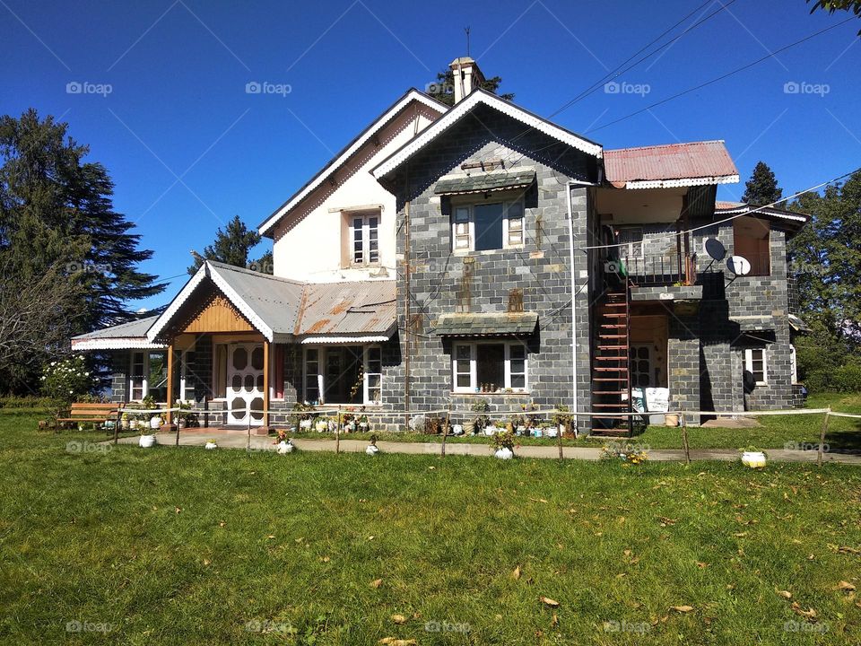 This exquisite photograph captures a magnificent house perched atop a hill, surrounded by lush greenery and commanding a breathtaking view. The elegant lines and timeless design of the house are highlighted by the natural beauty of the surroundings.