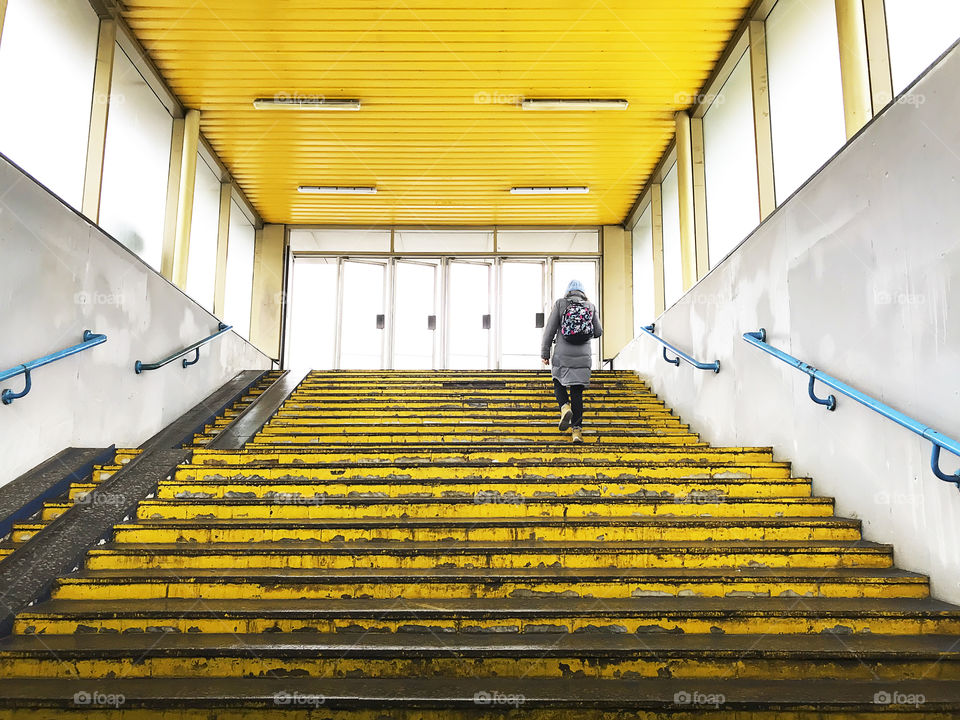 Young woman with a backpack walking by yellow steps upstairs 