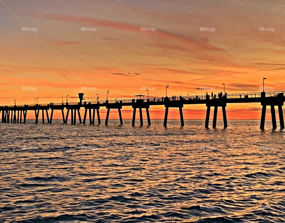 Some people are fishing and some people are photographing the sunset surrounded by the Gulf of Mexico