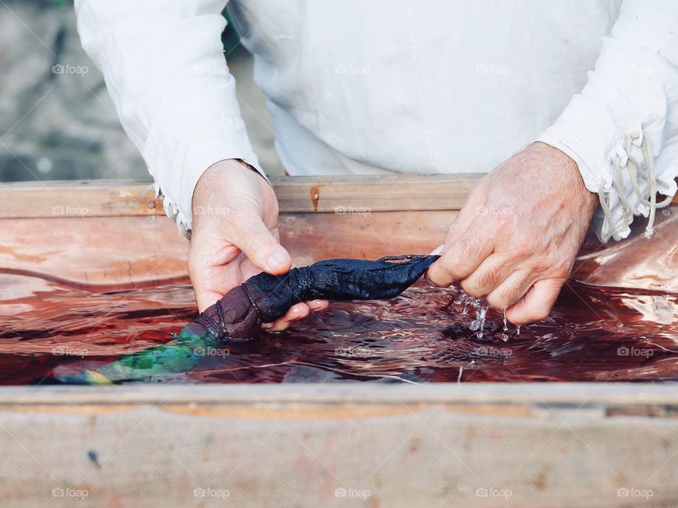 The man in the old national costume is showing a process of the hand dyeing fabric in Italy