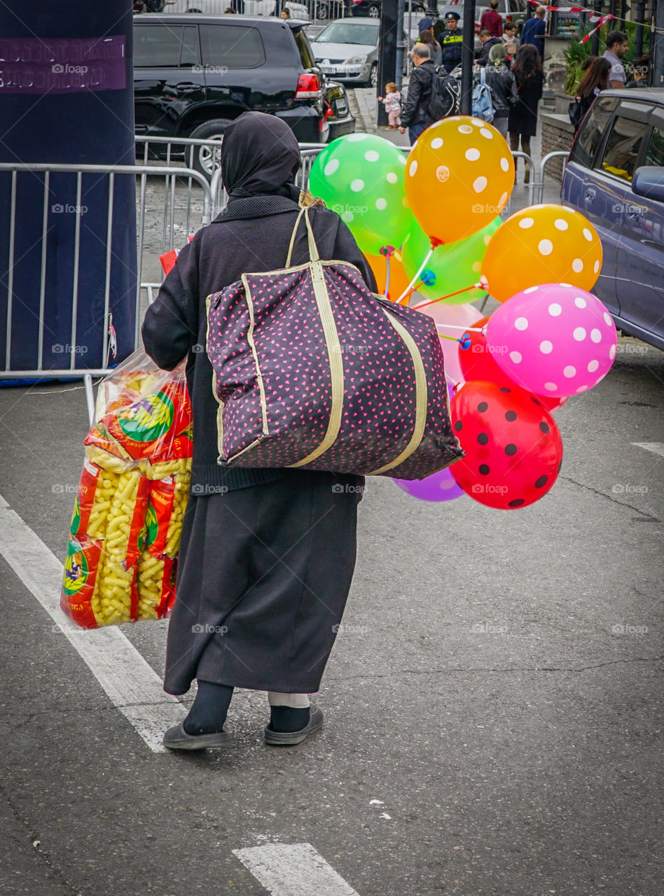 a poor women with colorful balloons and big bags comes from the streetmarket