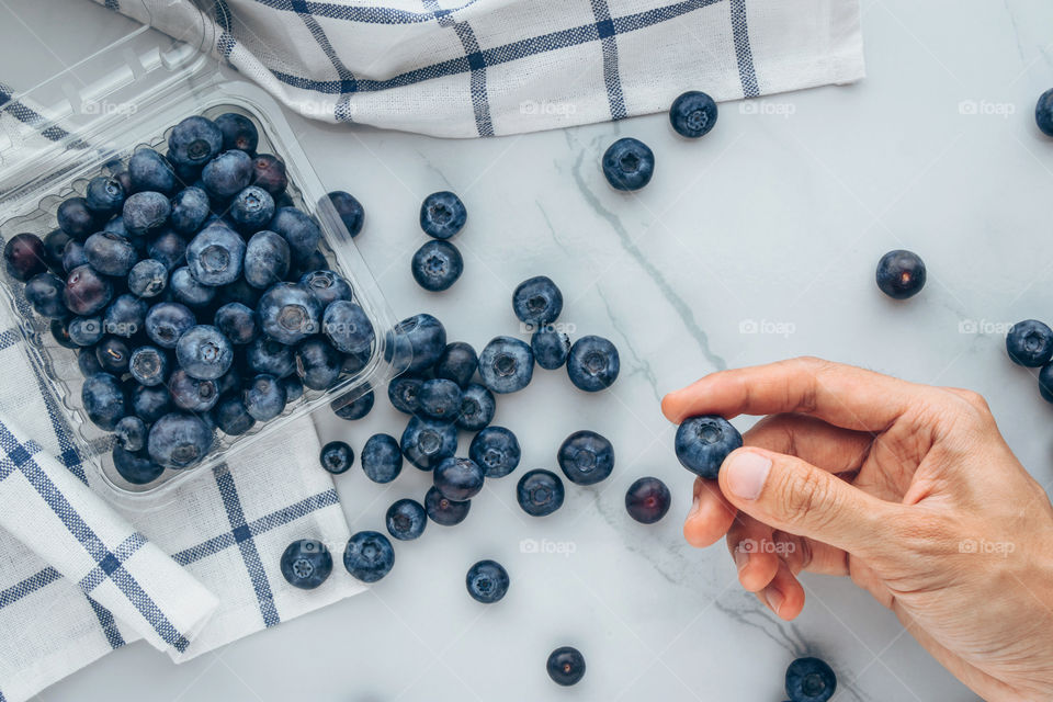 Hand picking organic fresh blueberries on a marble background 