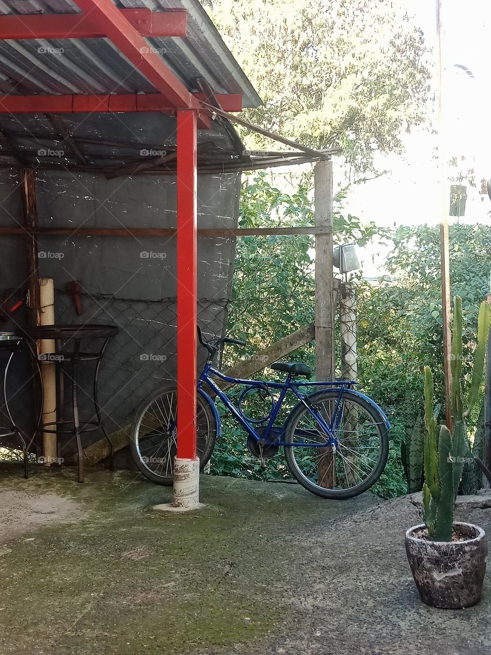 A blue bicycle by a natural fence and near a red pole