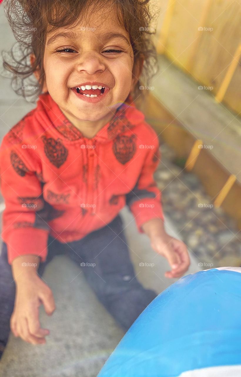 Happy toddler plays with beach ball, toddler playing outside, toddler showing emotion of happiness, toddler laughing outside, cute toddler girl smiling, playing outside with beach balls, toddler laughing and smiling while playing outside