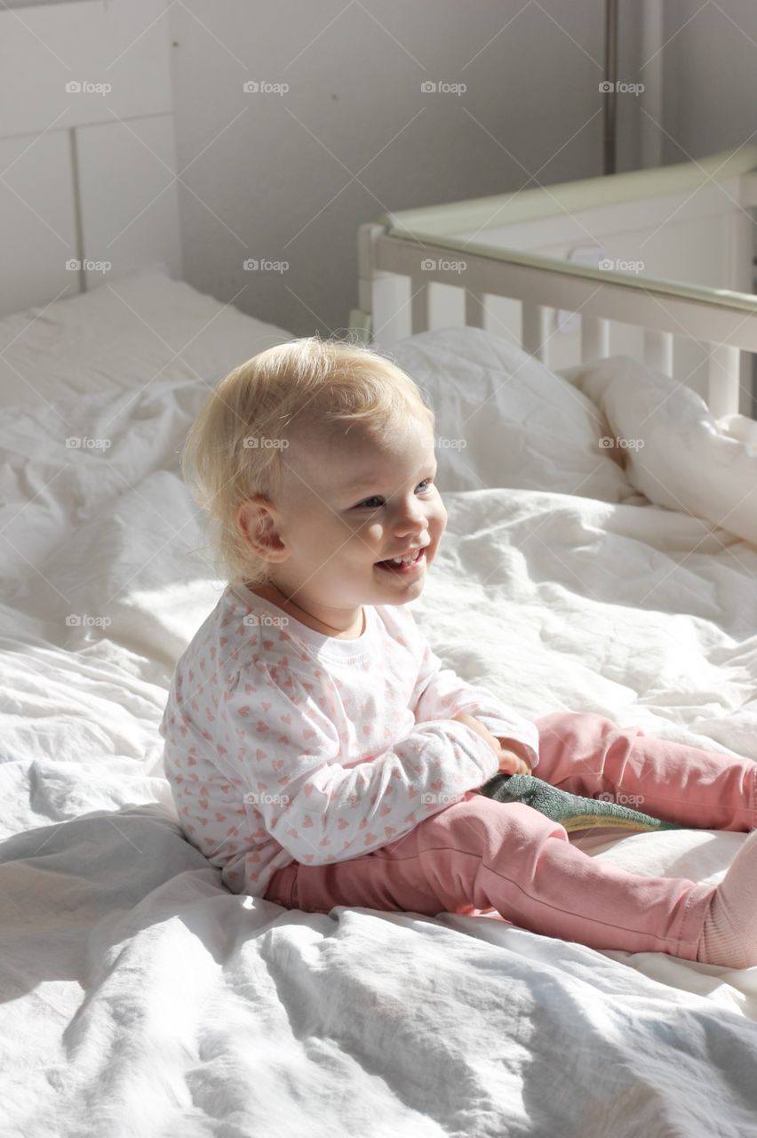 Happy baby girl laughing on a bed in the lights of a sun