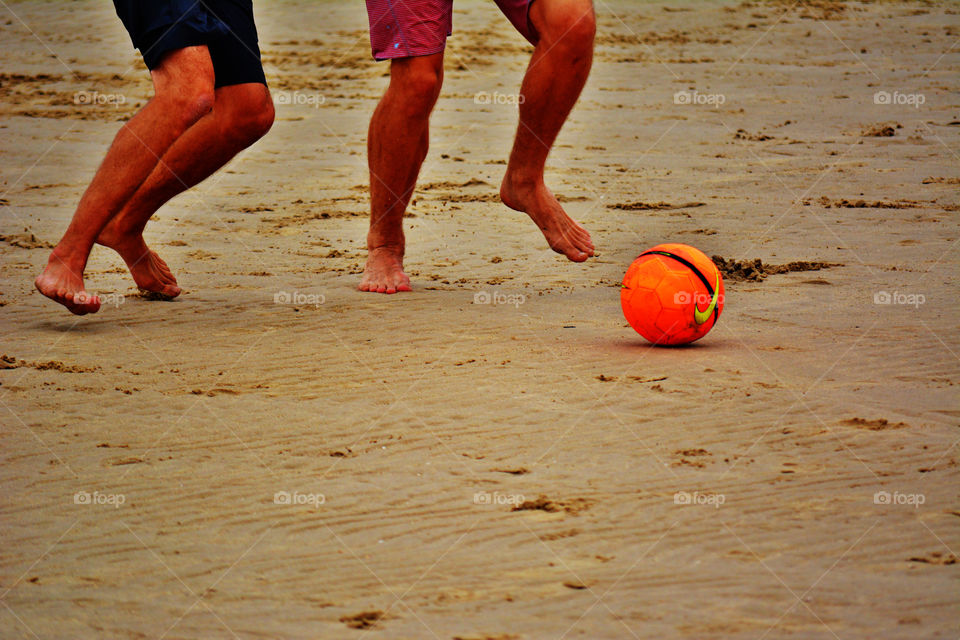 Footy. Men playing football at the beach.