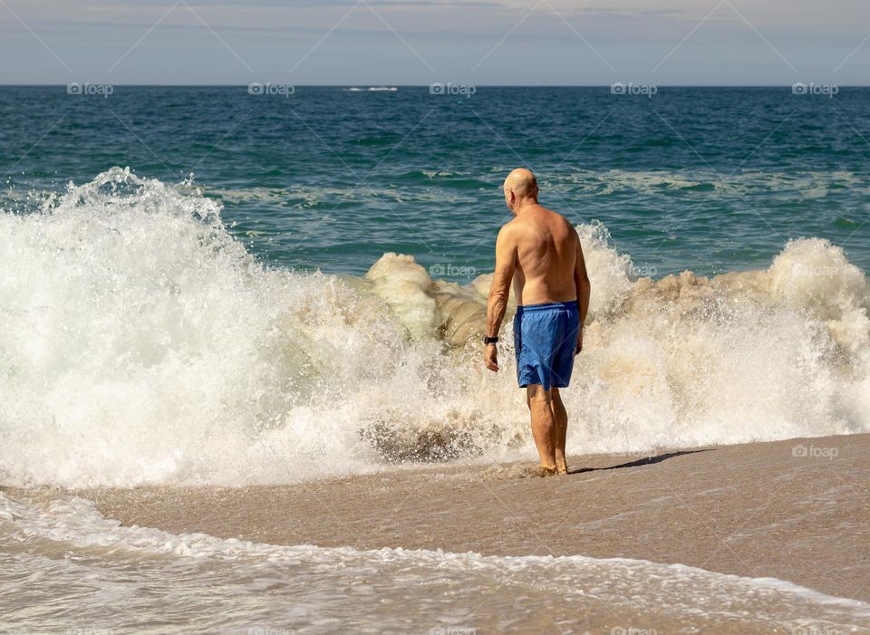 A man in swimwear considers a dip in the Atlantic Ocean at Nazaré, Portugal 
