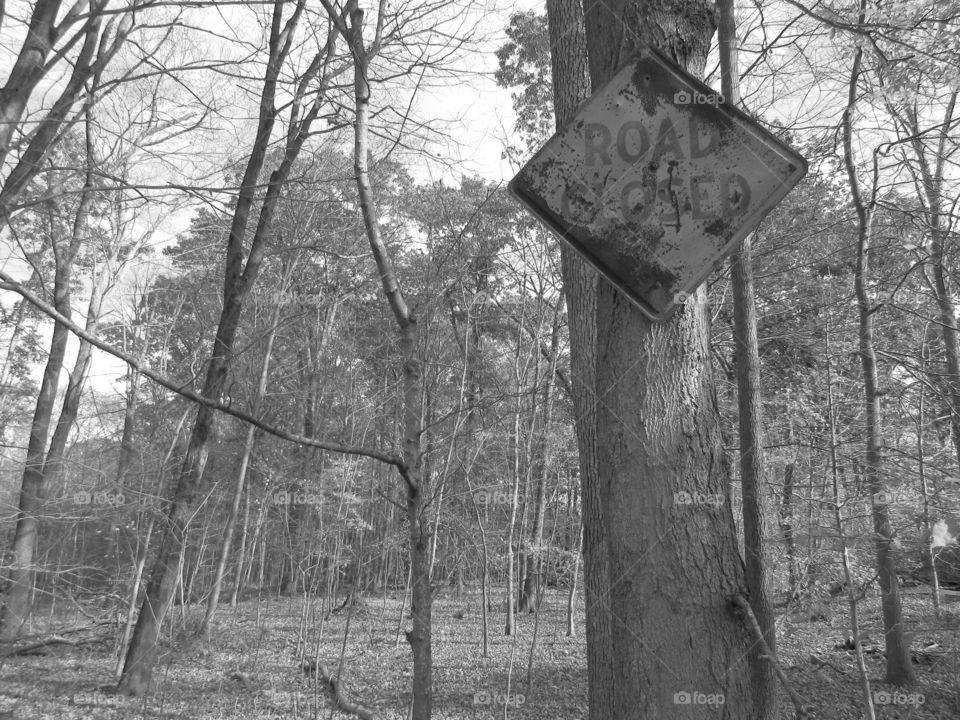 Black and white photo of a rusted road closed sign in the woods