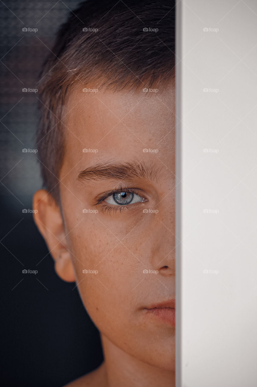 Close-up portrait of shy boy behind window frame