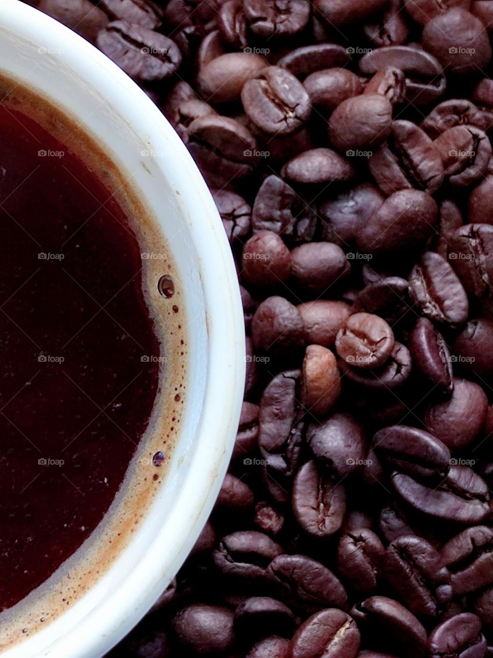 View from above. Half of white cup with black coffee and with coffee beans