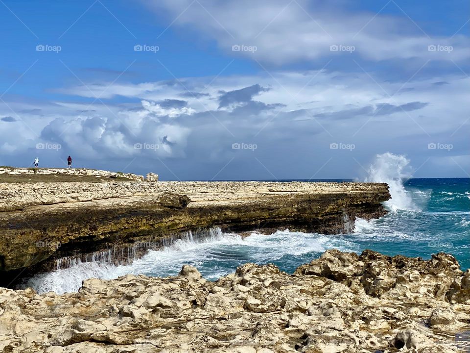 Waves crashing into a rocky outcrop while a person stands watching