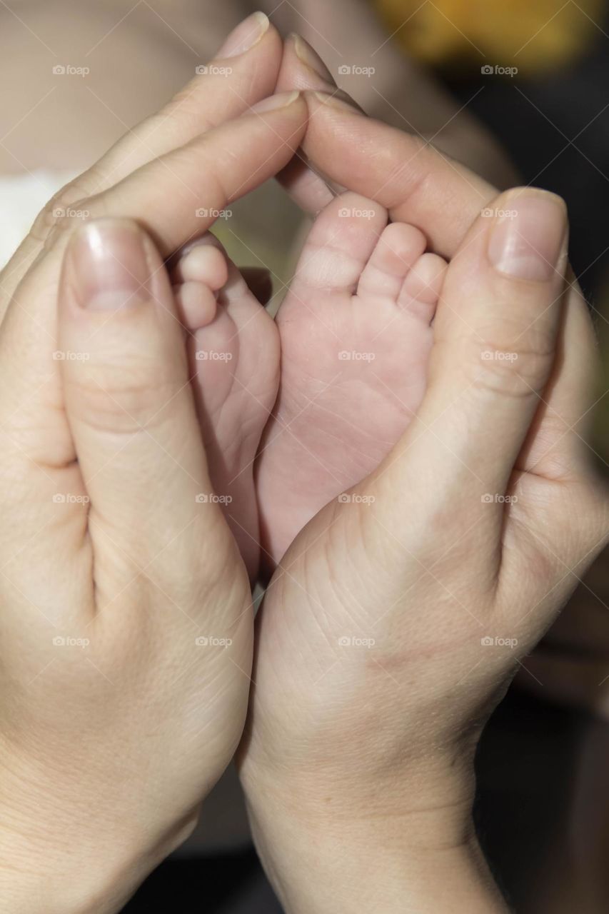 A happy mother in white holds the legs of a newborn baby in her hands. Lifestyle and newborn.