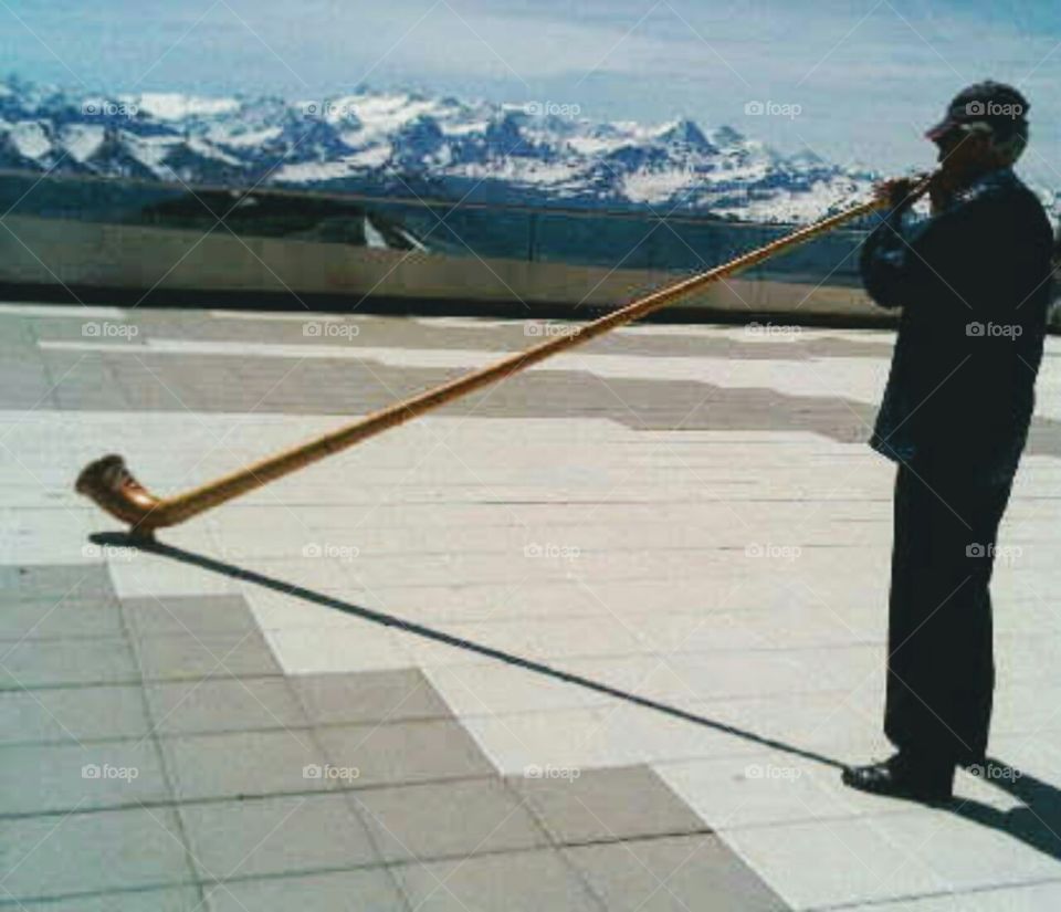 Swiss alphorn player overlooking Alps.