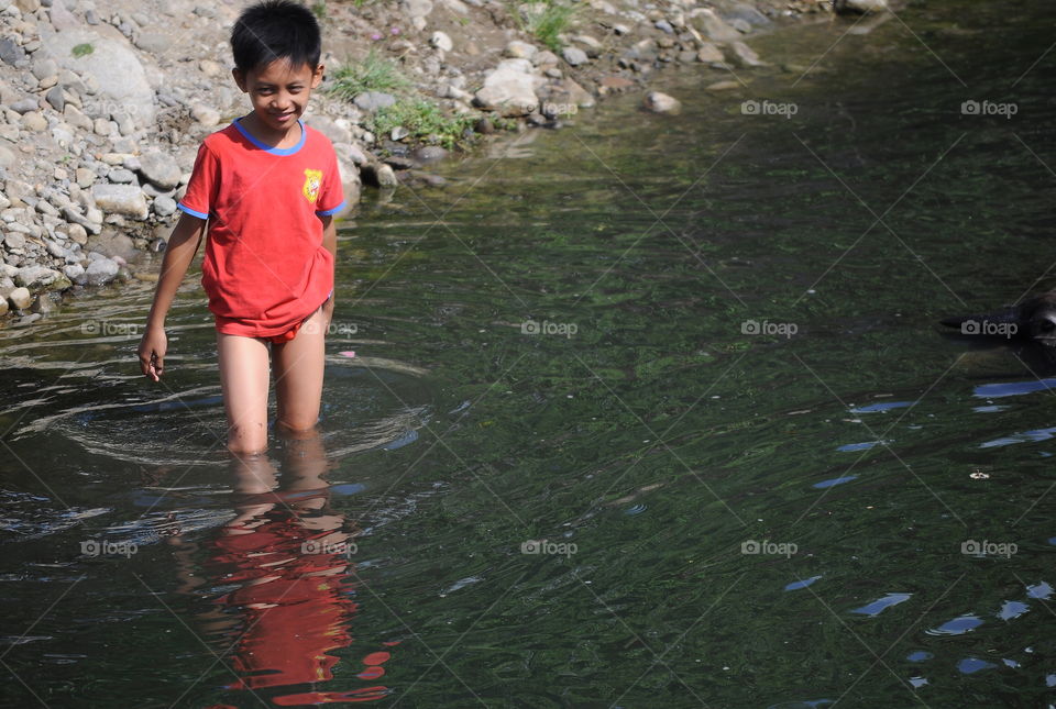 Happy teenager into the river. The teenager with red shirt good in an expression for reach the river. Here's long of time to the village of where's pboto taken got rain. What dry season ! And that's river for rare with the water's running.