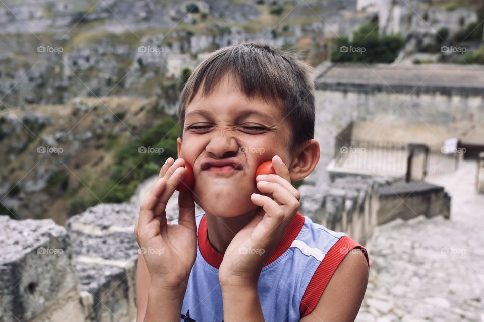 School boy have fun with small tomatoes, monkey face 