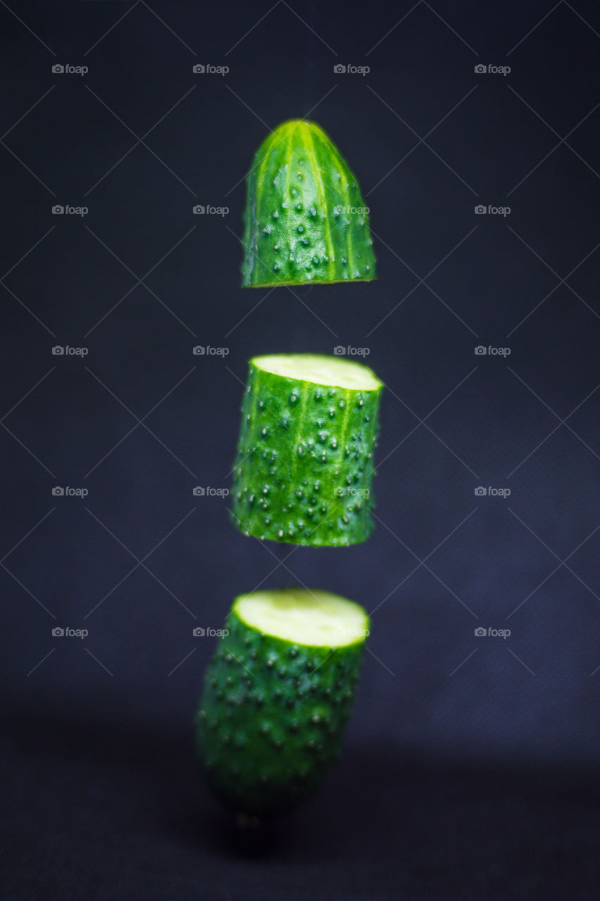 Close-up of a cucumber cut into three parts in the air on a black background.