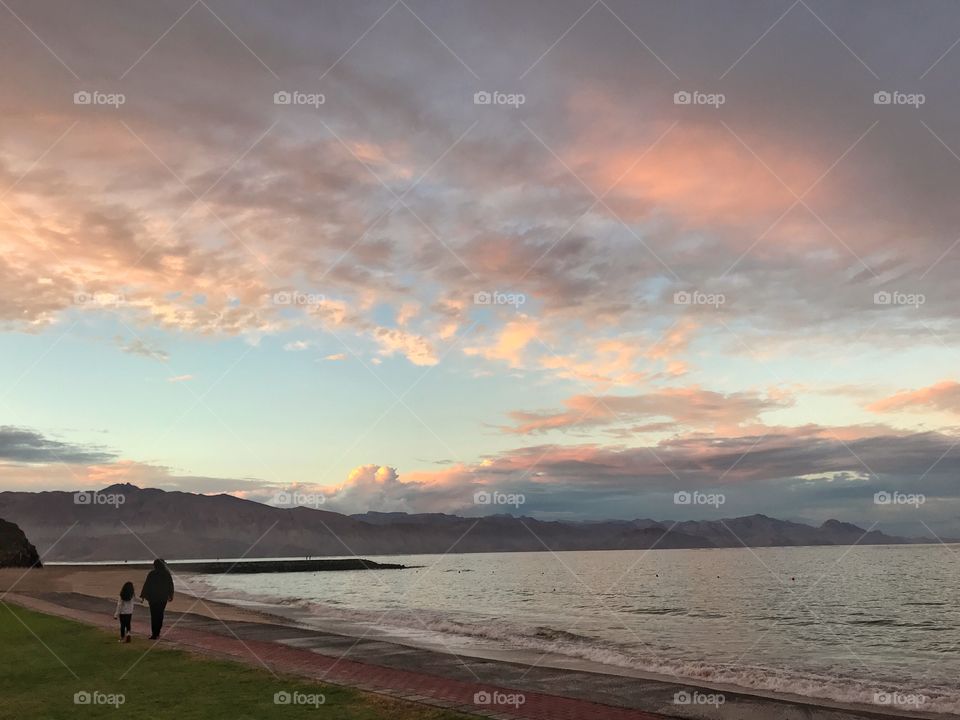 Mother and child taking a walk on the empty beach with a mountain backdrop during the sunset golden hour