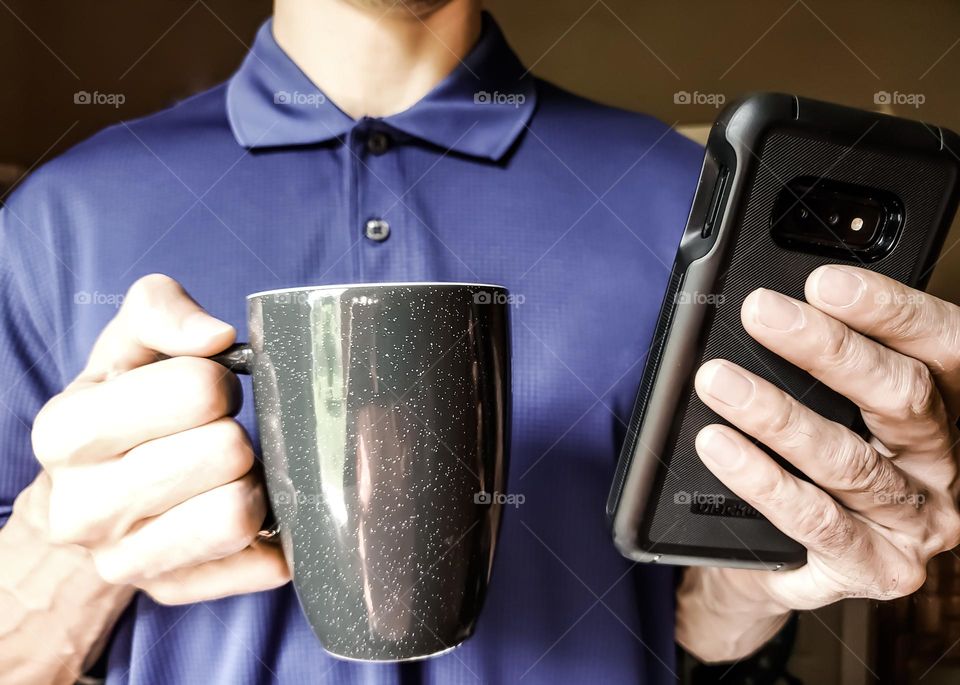 Closeup of a man wearing a polo shirt and drinking coffee while on his cell phone.