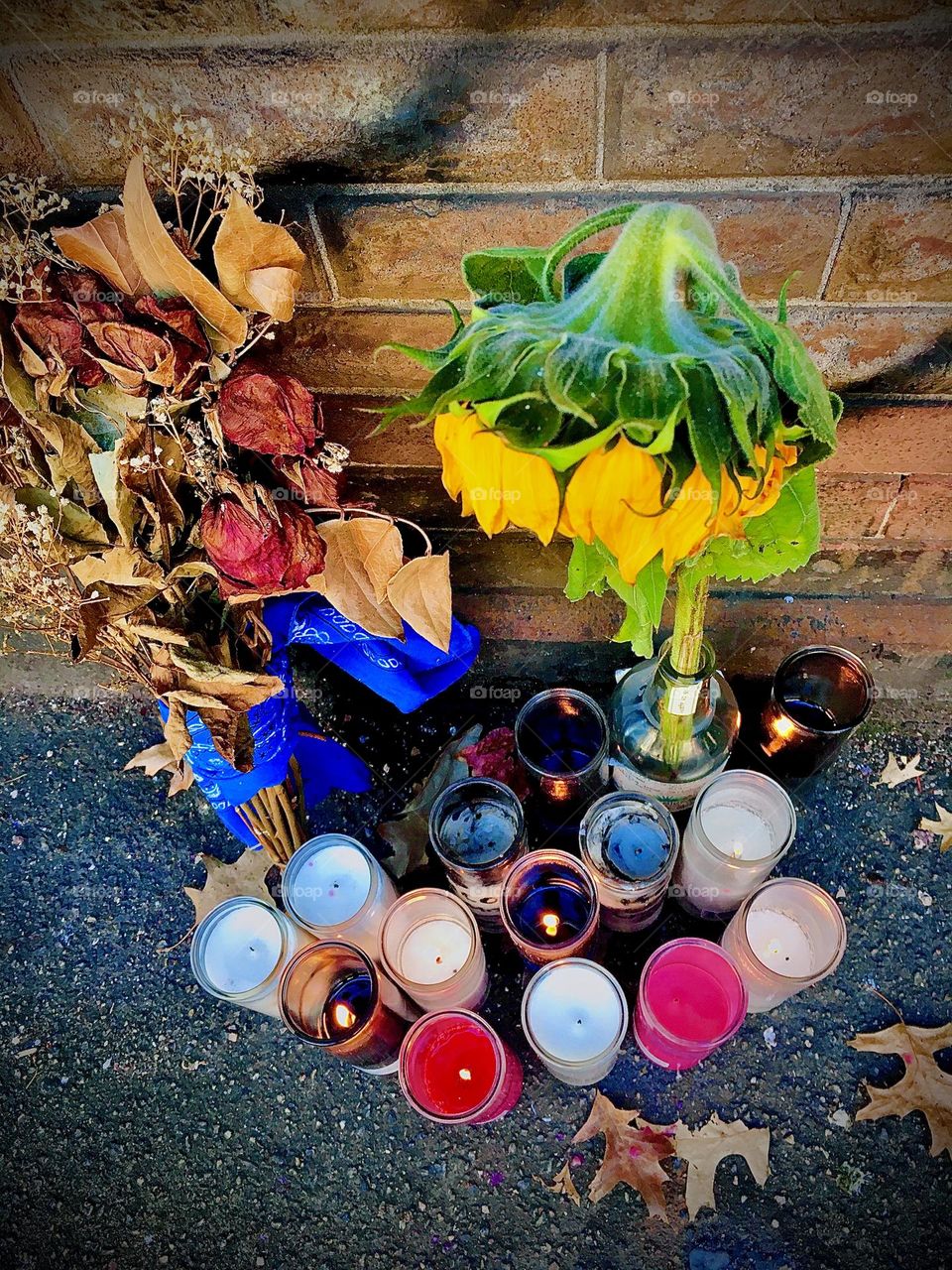 A wilted sunflower bends its „heads “ over votive glass candles, next to it a dried bouquet of roses. This is part of a public memorial for a Fort Greene, Bklyn man named „Nico“ shot to death at a local deli in 2020. Hypnotic Productions