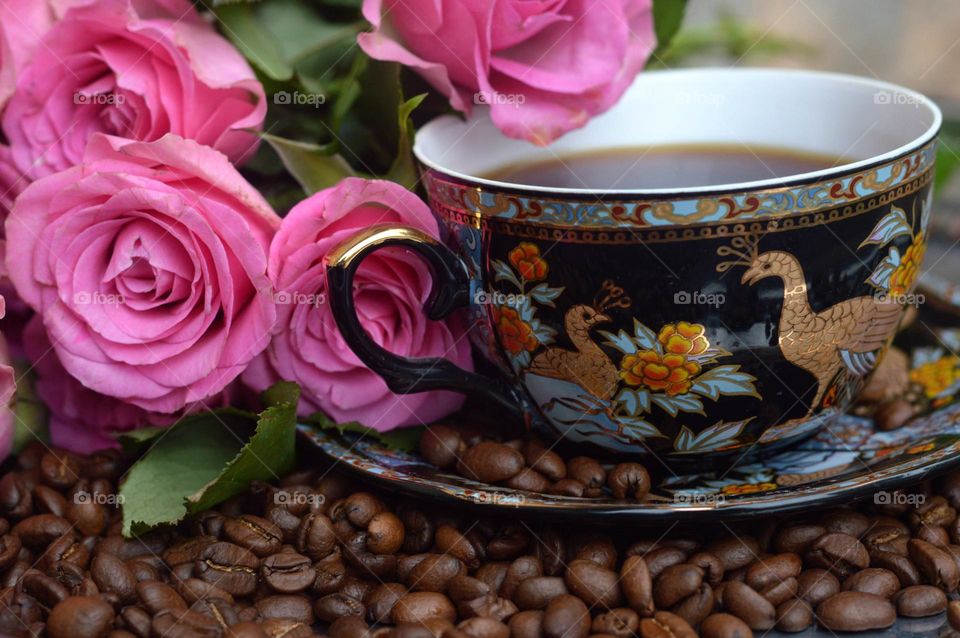 morning coffee in the beautiful cup surounded with coffee beans and pink roses.