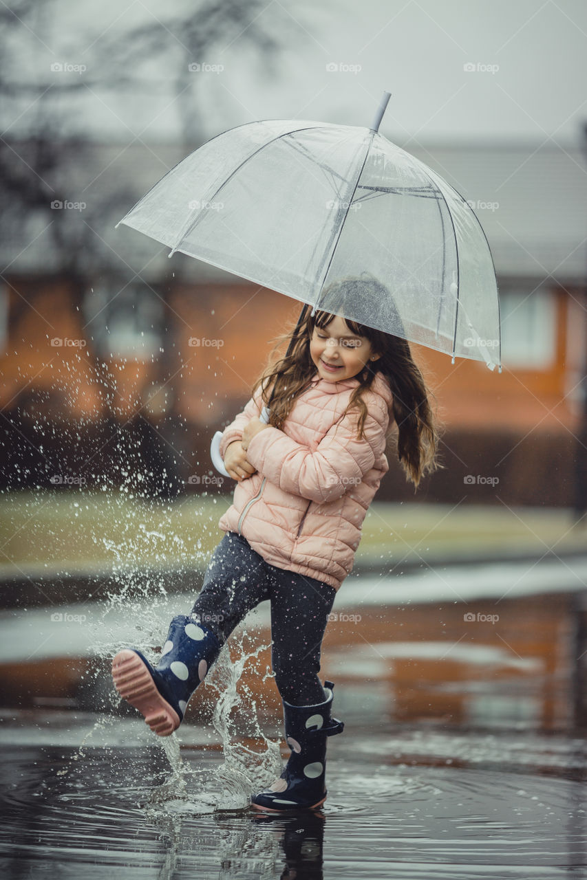 Little girl with umbrella and waterproof boots have fun in puddle 