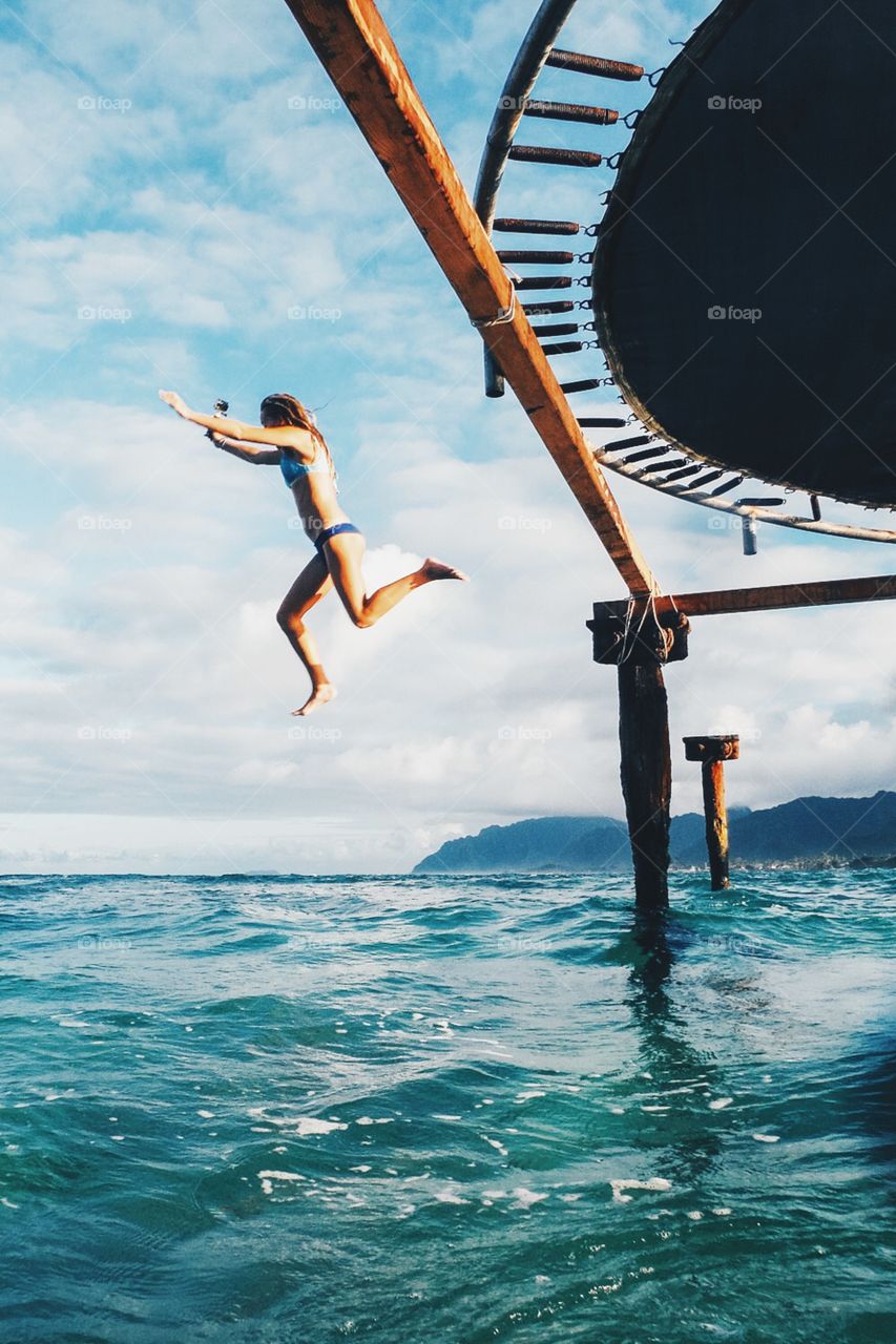 Girl jumps off a trampoline in the middle of the ocean.
