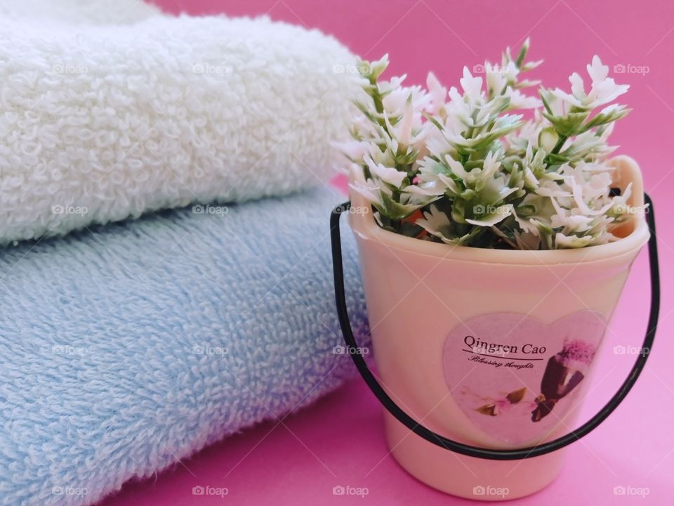 towel on a pink background and flowers in a bucket