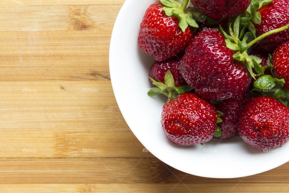Bright, ripe strawberries lie in a white bowl on a wooden surface.