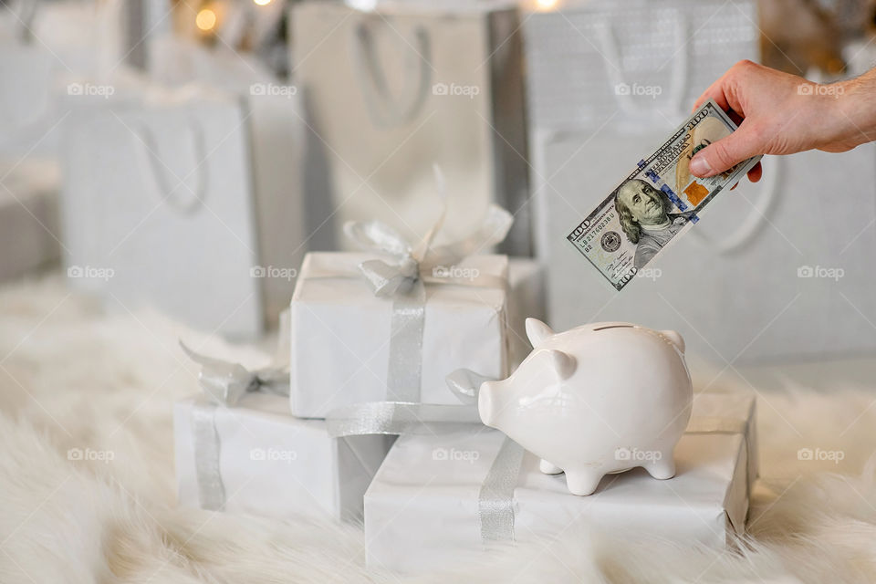 piggy bank with 100 dollars banknote in festive New Year atmosphere of scenery. Magical bokeh with Christmas tree and bright lights.