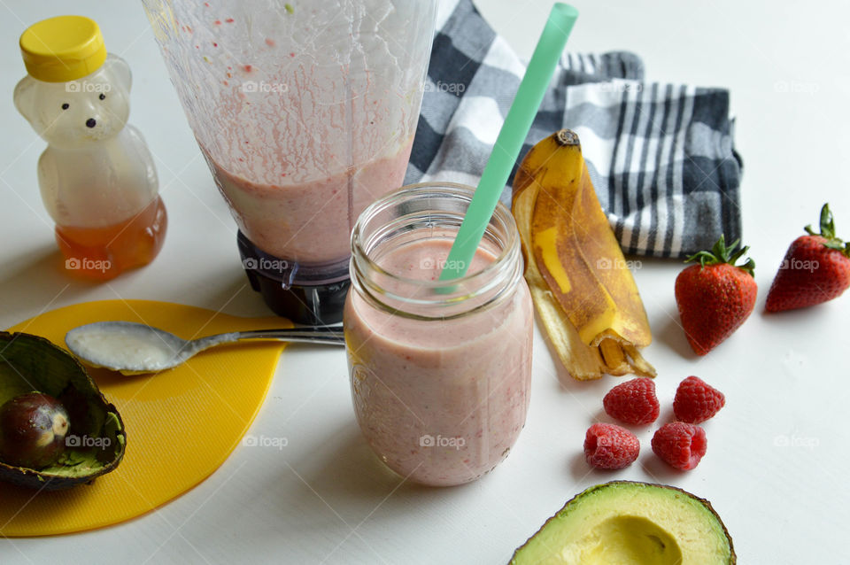 Fresh fruit smoothie in a glass with banana peel, avocado, raspberries, strawberries and honey bear