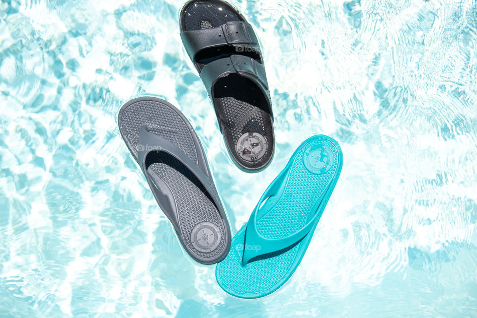Flat lay of women's sandals floating on top of an outdoor swimming pool