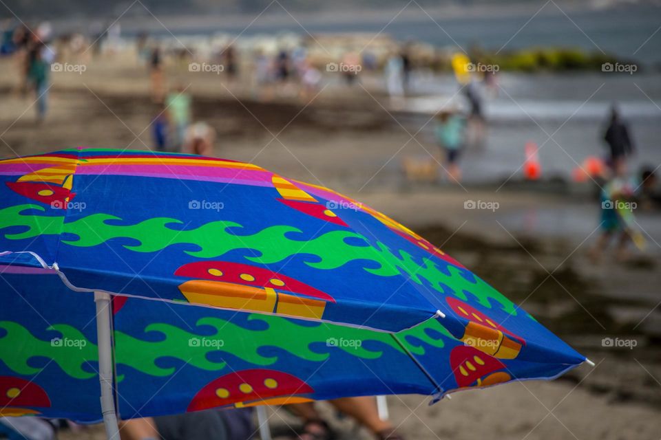 Colorful umbrella on the beach on a warm summer day in Capitola California with families enjoying the sun, surf, and sand