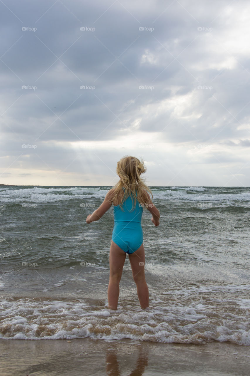 Young girl playing at the beach of Tylösand outside Halmstad in Sweden. It's about to get stormy weather but the girl is having fun swimming and playing in the water.