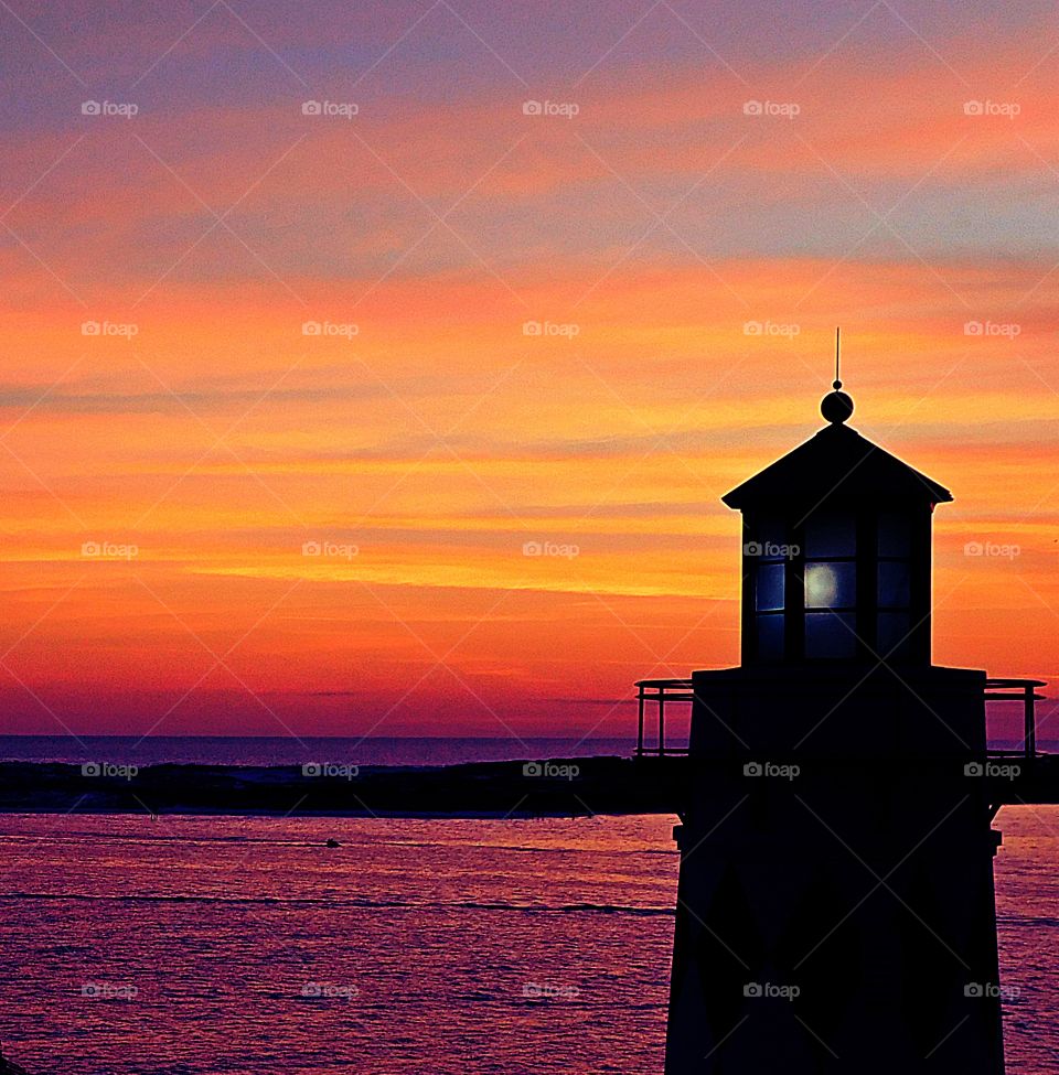The lighthouse beacon and the credulous sunset are the last light of the day.  The lighthouse helps water vessels navigate their way home while the descending sunset gives off magnificent colors.