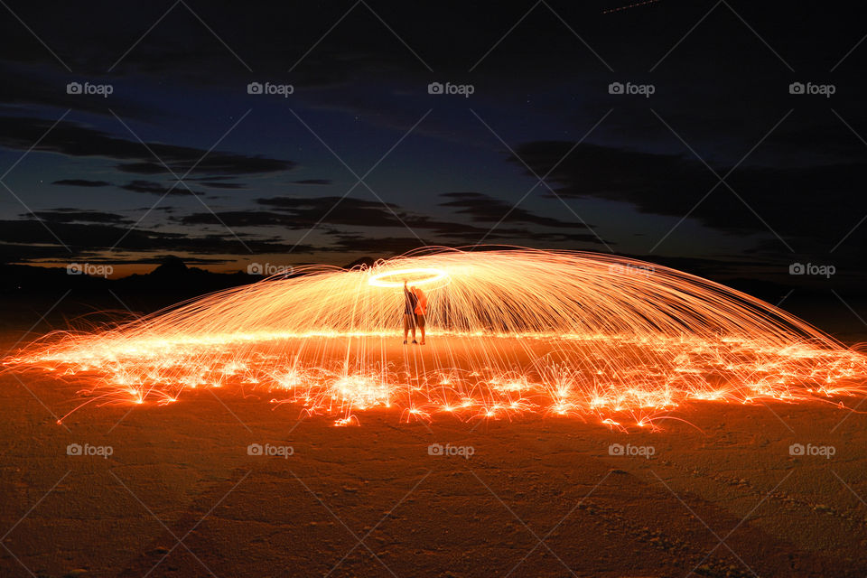 Long exposure photo of couple standing under the umbrella of flying sparks made with a help of spinning burning steel wool 