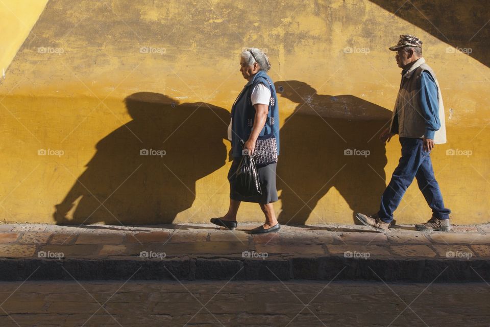 Two people with shadows leisurely walking against a building wall