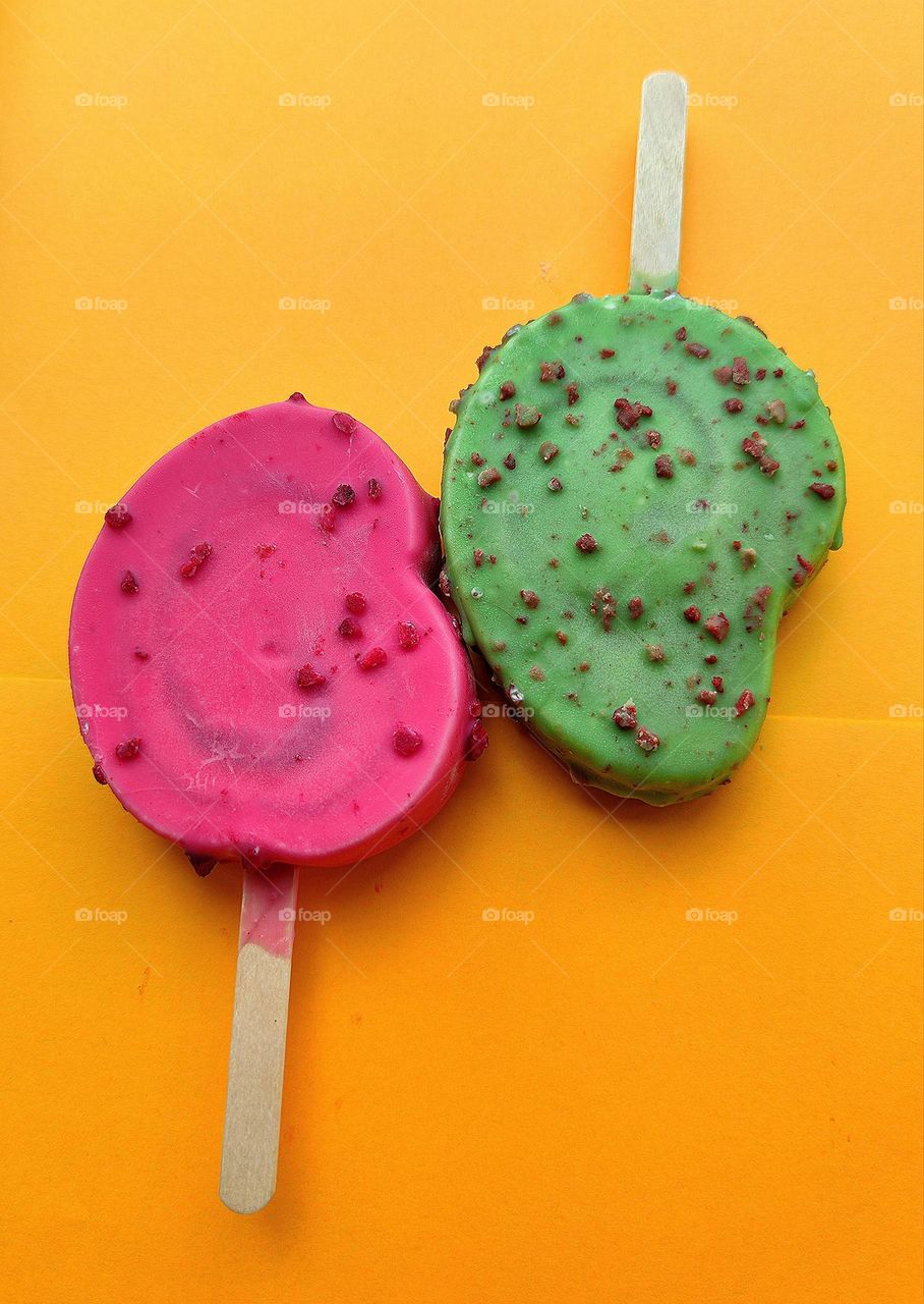 Summer. Time to cool off. On an orange background are two ice creams: red raspberry with raspberry pieces and green kiwi with chocolate pieces. Contrast of colors and taste