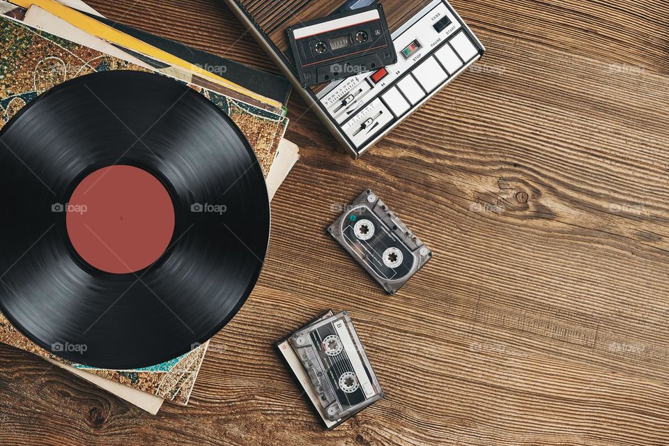 Vinyl records, cassette tapes and cassette recorder on wooden table. Retro music style. 80s music party. Vintage style. Analog equipment. Stereo sound. Back to the past